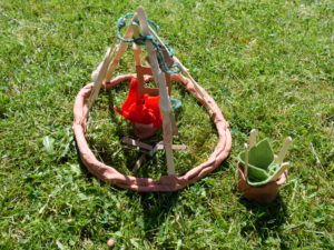 a model of tipee with a fire and a pot made from clay, wood and felt sitting on grass