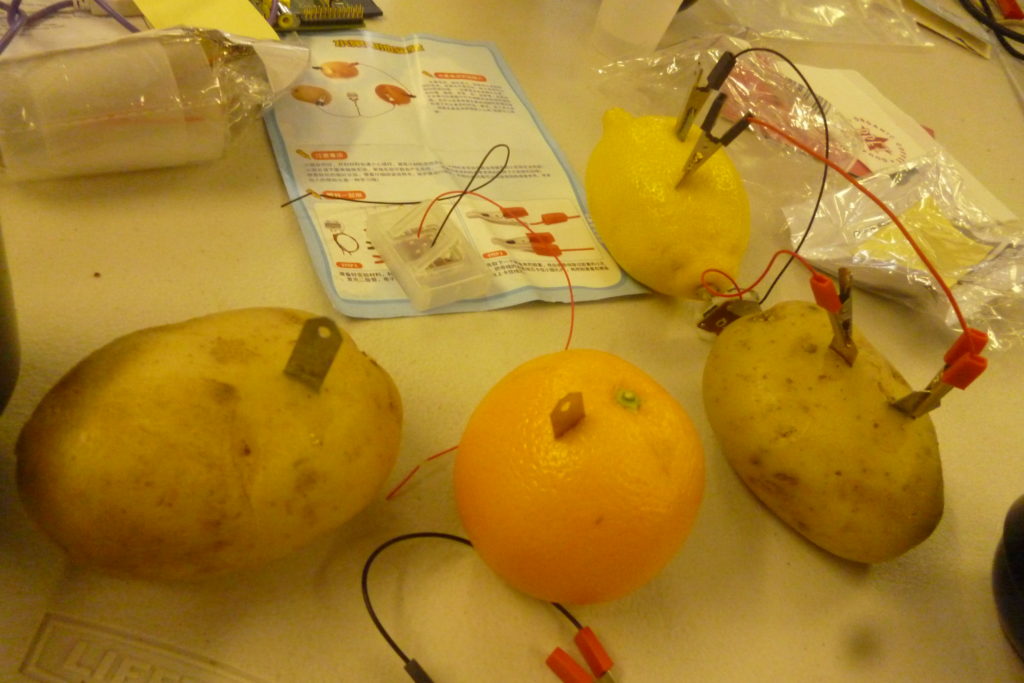two potatos, orange, lemon connected by cables zinc and copper to a clock