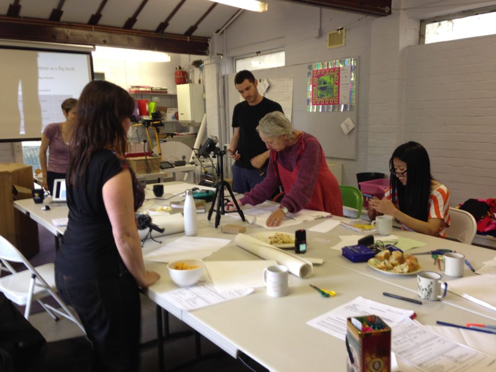 3 workshop participants working around a table with Rachel and Esther Eidinow helping them