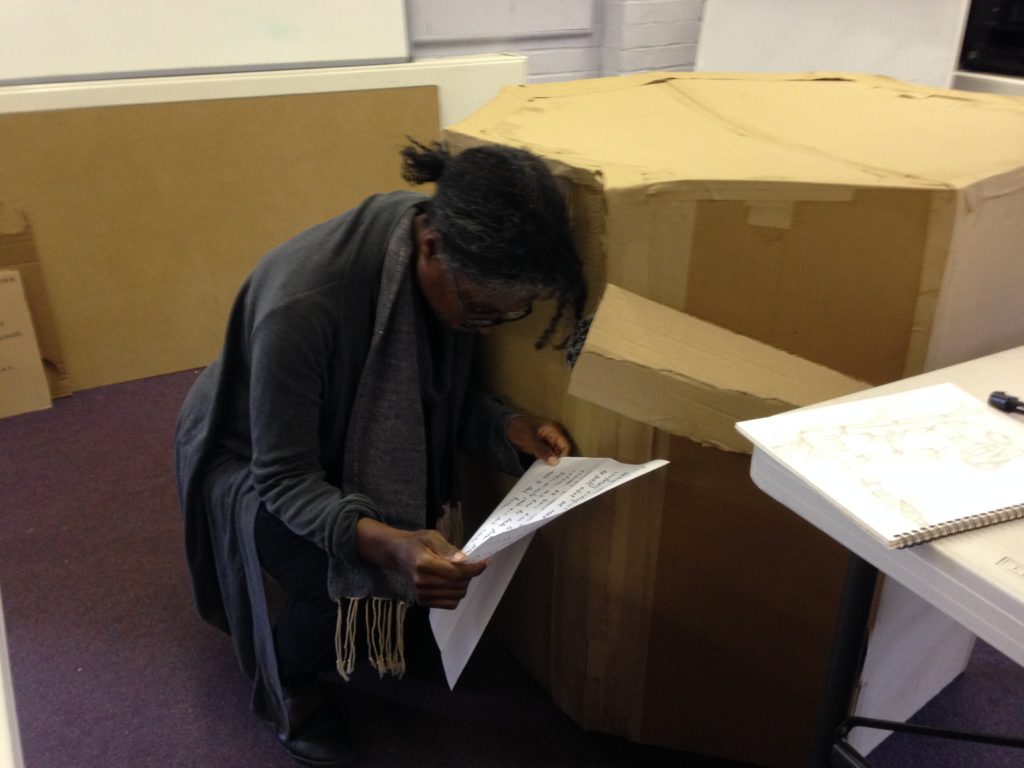 a workshop participant leaning against a cardboard model of the Future Machine reading from a large piece of paper into a cardboard trumpet