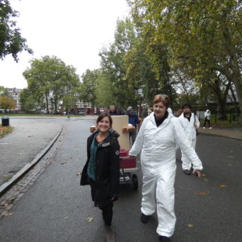 Rachel Jacobs and Ruth Catlow pulling the Future Machine uphill with the procession of people behind and Autumnal trees in Finsbury Park