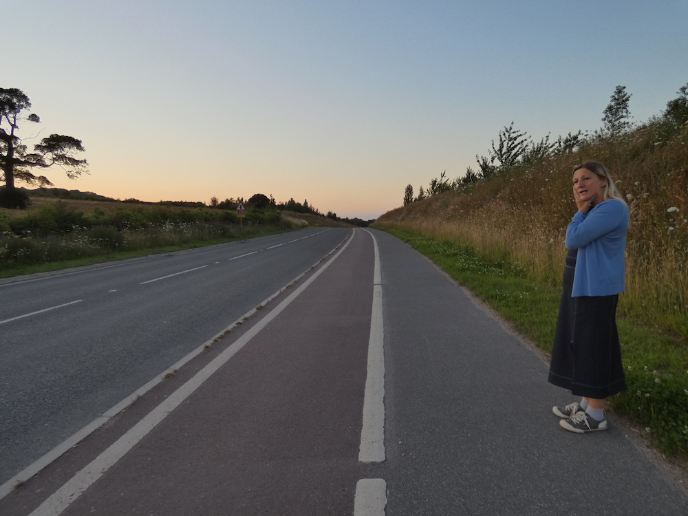 Caroline standing on the side of the empty bypass cutting through the fields above the village of Cannington