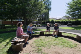 Rachel and three children from Cannington Primary School sitting on a bench in the playground surrounded by trees