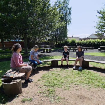 Rachel and three children from Cannington Primary School sitting on a bench in the playground surrounded by trees