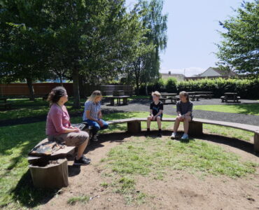 Rachel and three children from Cannington Primary School sitting on a bench in the playground surrounded by trees