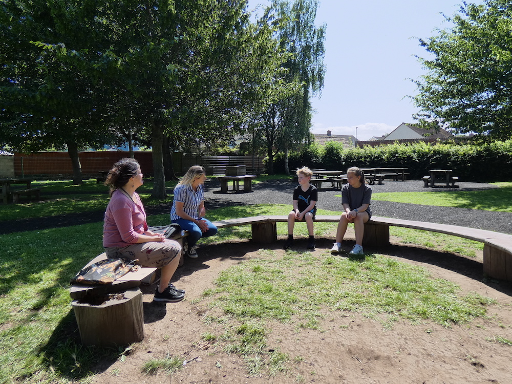 Rachel and three children from Cannington Primary School sitting on a bench in the playground surrounded by trees