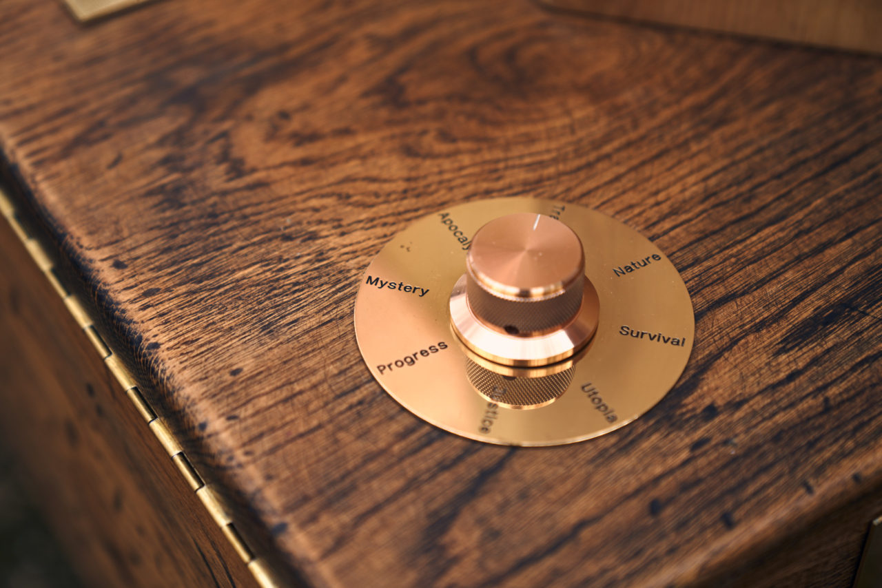 a brass dial on Future Machine's distressed oak base with the words nature, survival, utopia, Justice, progress, mystery and apocalypse inscribed in a brass disc around the dials