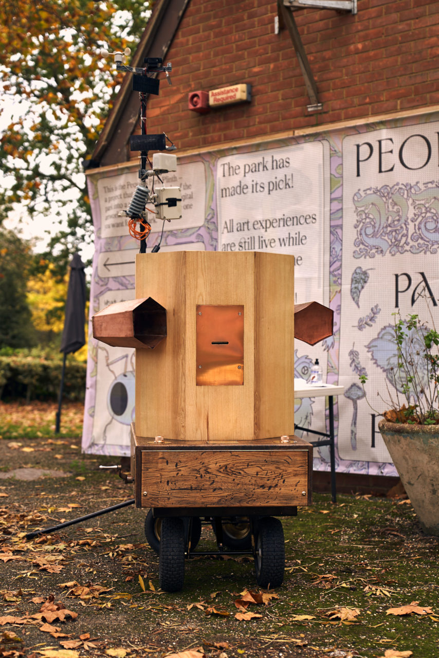 Future Machine in the front and Furtherfield Gallery behind with posters wrapped around the gallery. Autumnal trees in the background