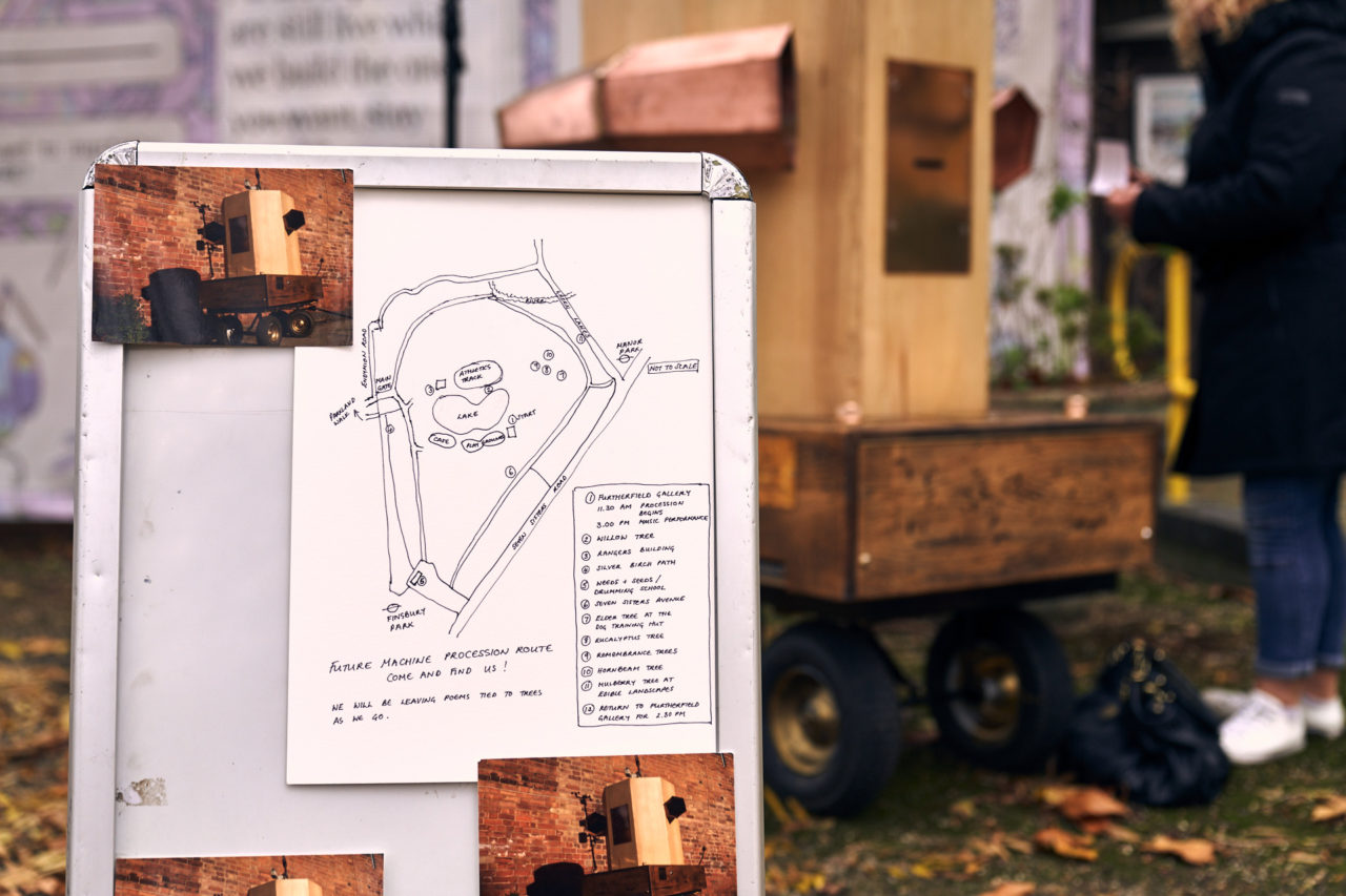 An A board with postcards of the Future Machine and a drawn map of Finsbury Park with details of the stopping points. The Future Machine in the background with someone holding a printed message in their hand