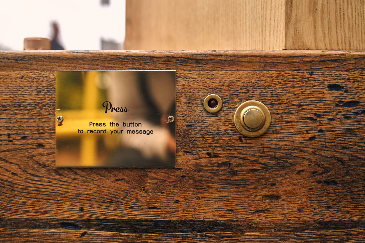 A brass sign on the side of the Future Machine with Press - press the button to record your message, a red light surrounded by a brass ring and a brass button