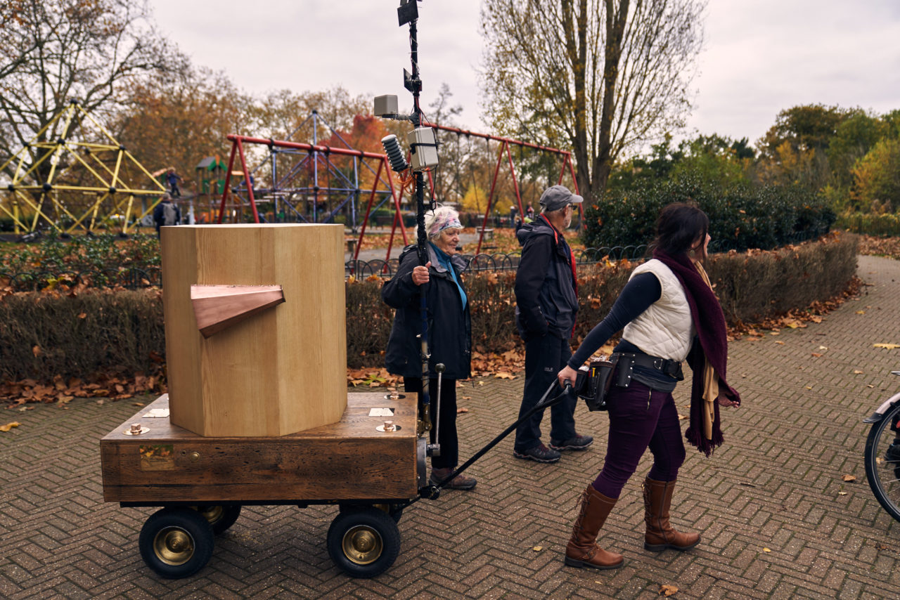 Rachel pulling Future Machine, a woman holds the weather ole and a man walks alongside, with the playground and autumn trees in the background