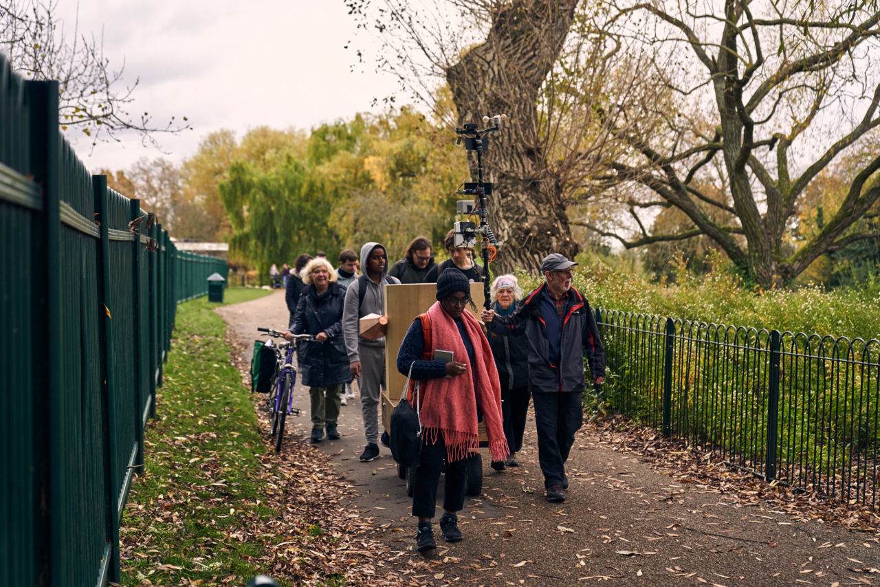 The procession walking past willow trees, with metal fencing on each side