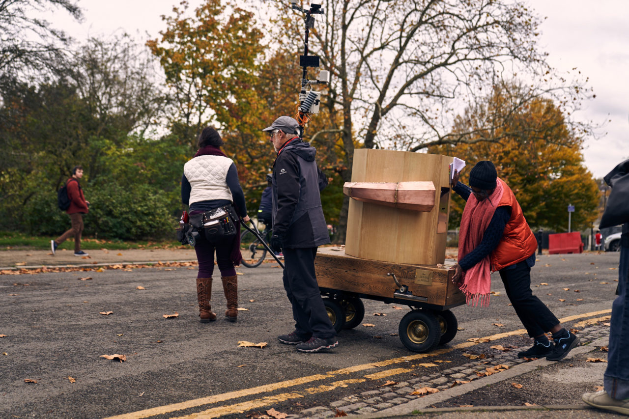 Esi pushing the Future Machine across a road with a man holding the weather pole and Rachel pulling