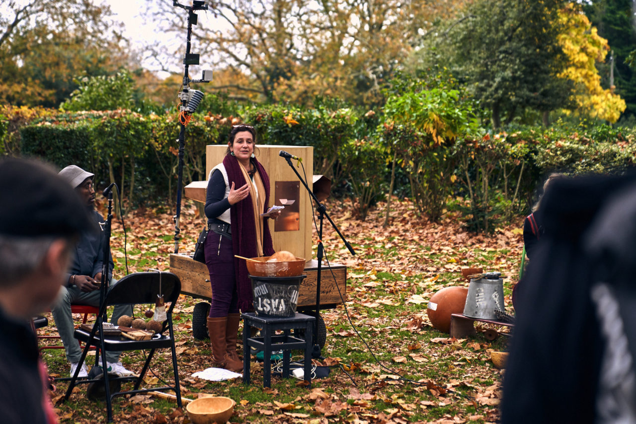 Rachel speaking into a microphone next to the Future Machine and a water bowl, next to Miles Ncube surrounded by autumn leaves and trees