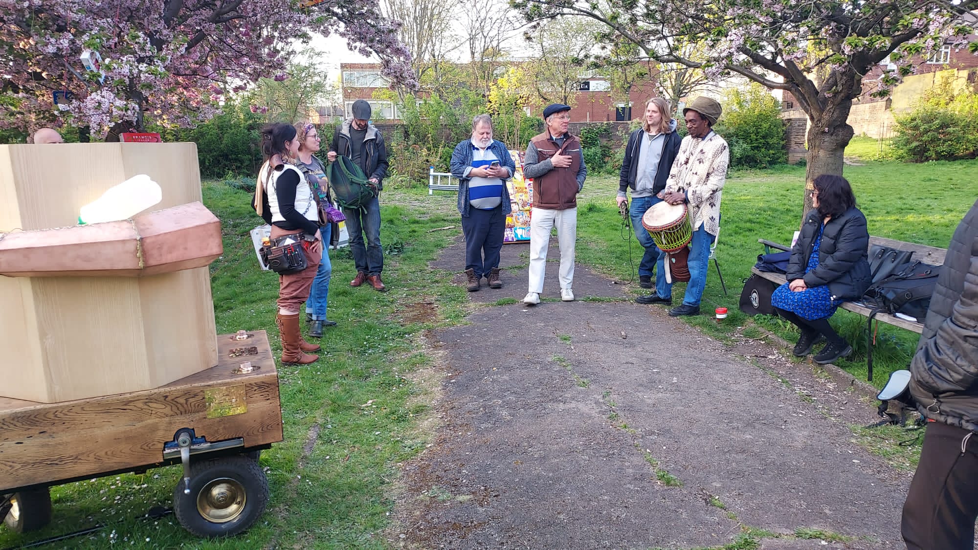 people standing around Frank talking under the blossom trees, someone sitting on the bench and Future Machine in the front