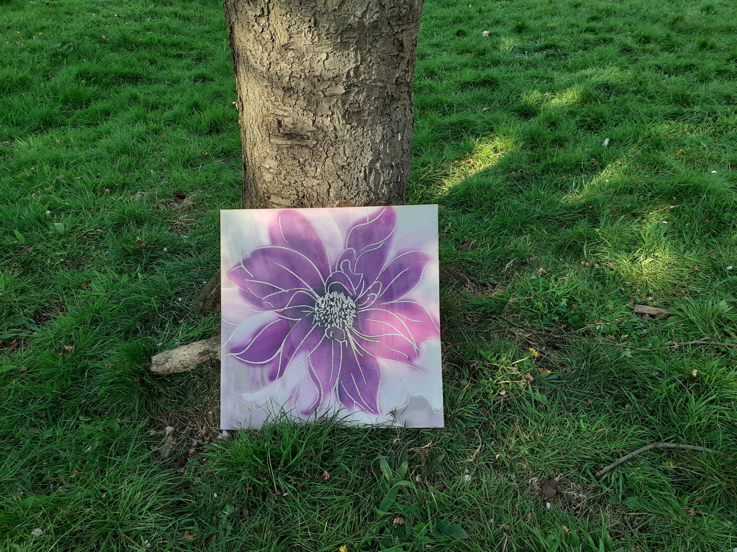 a painting of a pink flower underneath the tree. shadows and light on the green grass