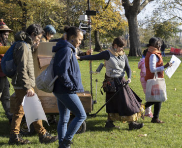 Future Machine being pulled by it's artist companion alongside a procession of five people. Autumn trees in the background.