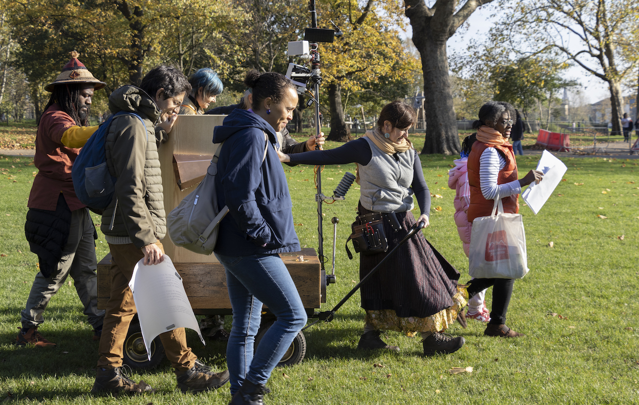 Future Machine being pulled by it's artist companion alongside a procession of five people. Autumn trees in the background.