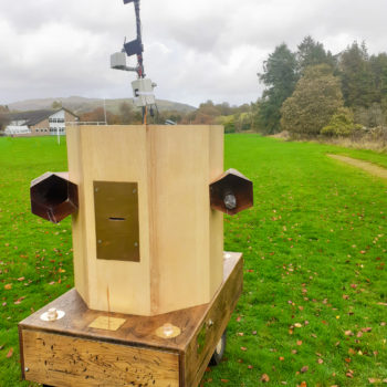 Future Machine with the weather station at the back, fells in the distance, trees and grass