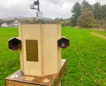 Future Machine with the weather station at the back, fells in the distance, trees and grass