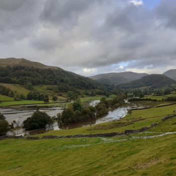 Troutbeck valley flooded, with green fields above the water and mountains and sky in the distance