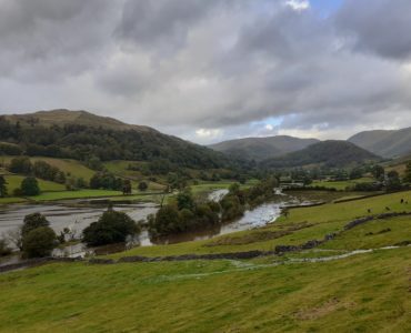 Troutbeck valley flooded, with green fields above the water and mountains and sky in the distance