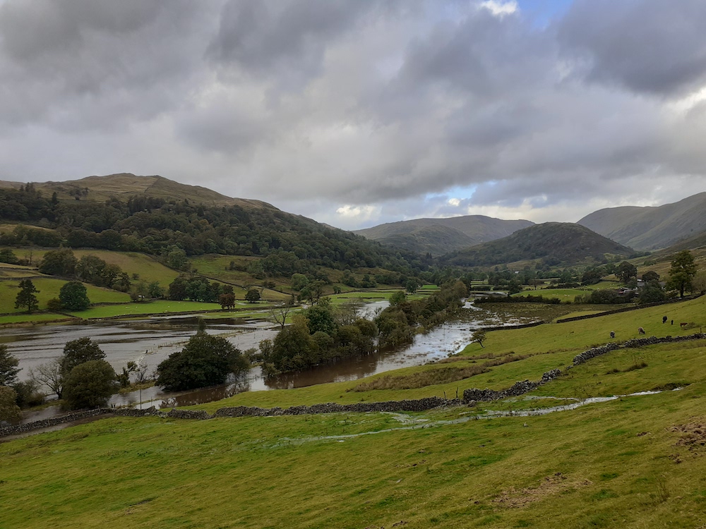 Troutbeck valley flooded, with green fields above the water and mountains and sky in the distance