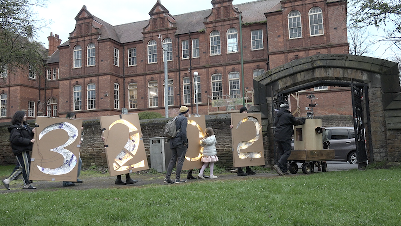 Future Machine being pushed through the gate with the lit up 2023 sign being carried by people behind. Primary in the background.