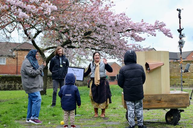 A family listening to the artist companion talking next to the Future Machine, and a sign saying Speak to the Future