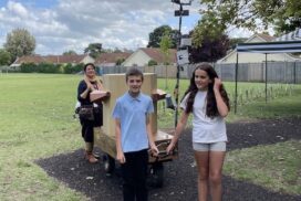 Two children pulling the Future Machine under a cloudy and blue sky with Rachel in the background