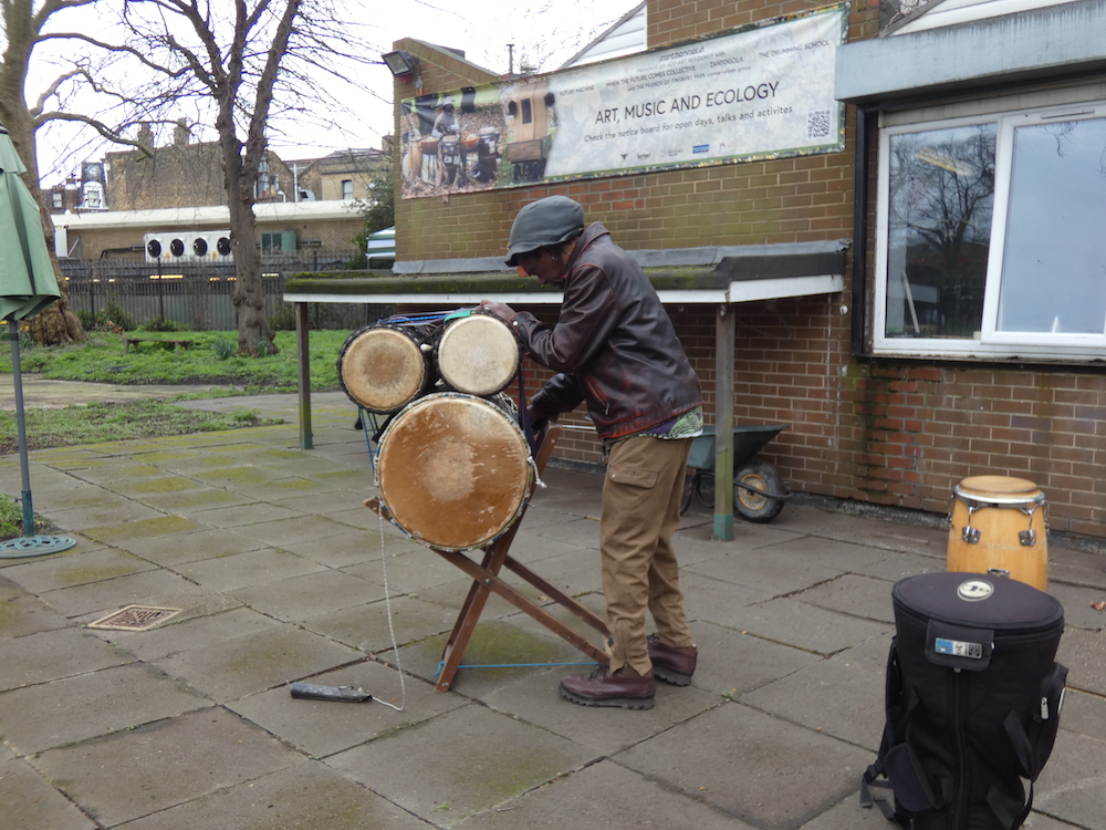 Alex, drums and Furtherfield Commons with a banner in the background about the residency