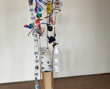 Sculpture of plants and creatures made of rubbish in a small cardboard stand.
