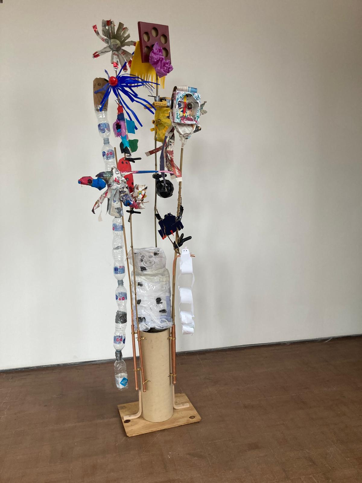 Sculpture of plants and creatures made of rubbish in a small cardboard stand.