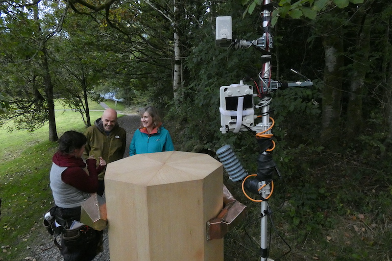 a couple, Future Machine and Future Machine's companion talking, a close up of the weather pole