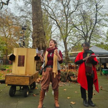 Rachel talking next to Esi watching with Future Machine and trees behind them