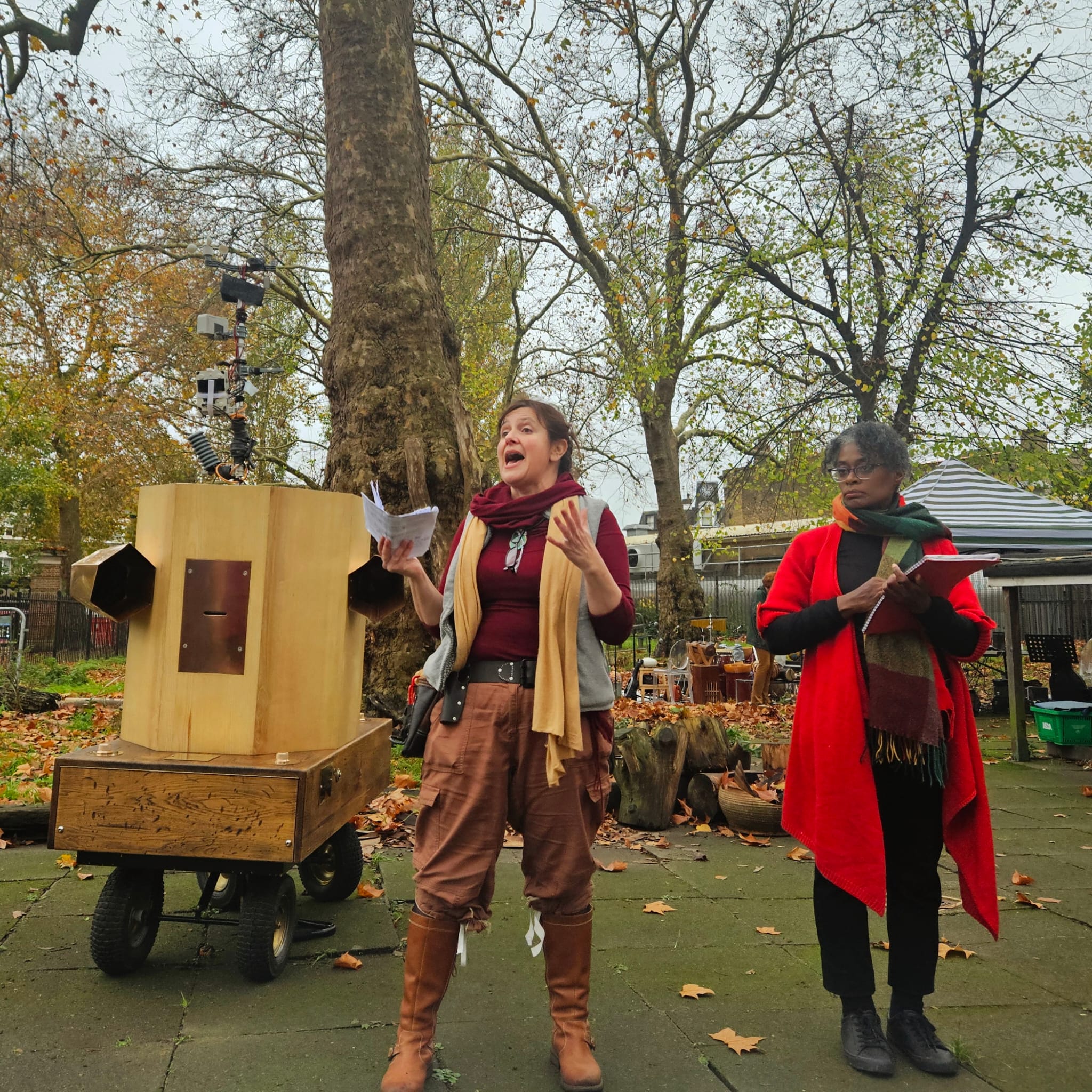 Rachel talking next to Esi watching with Future Machine and trees behind them