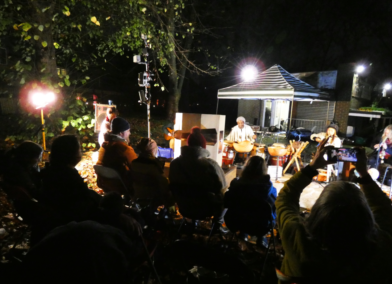 audience sitting down with The Rainmakers playing music and Future Machine in front