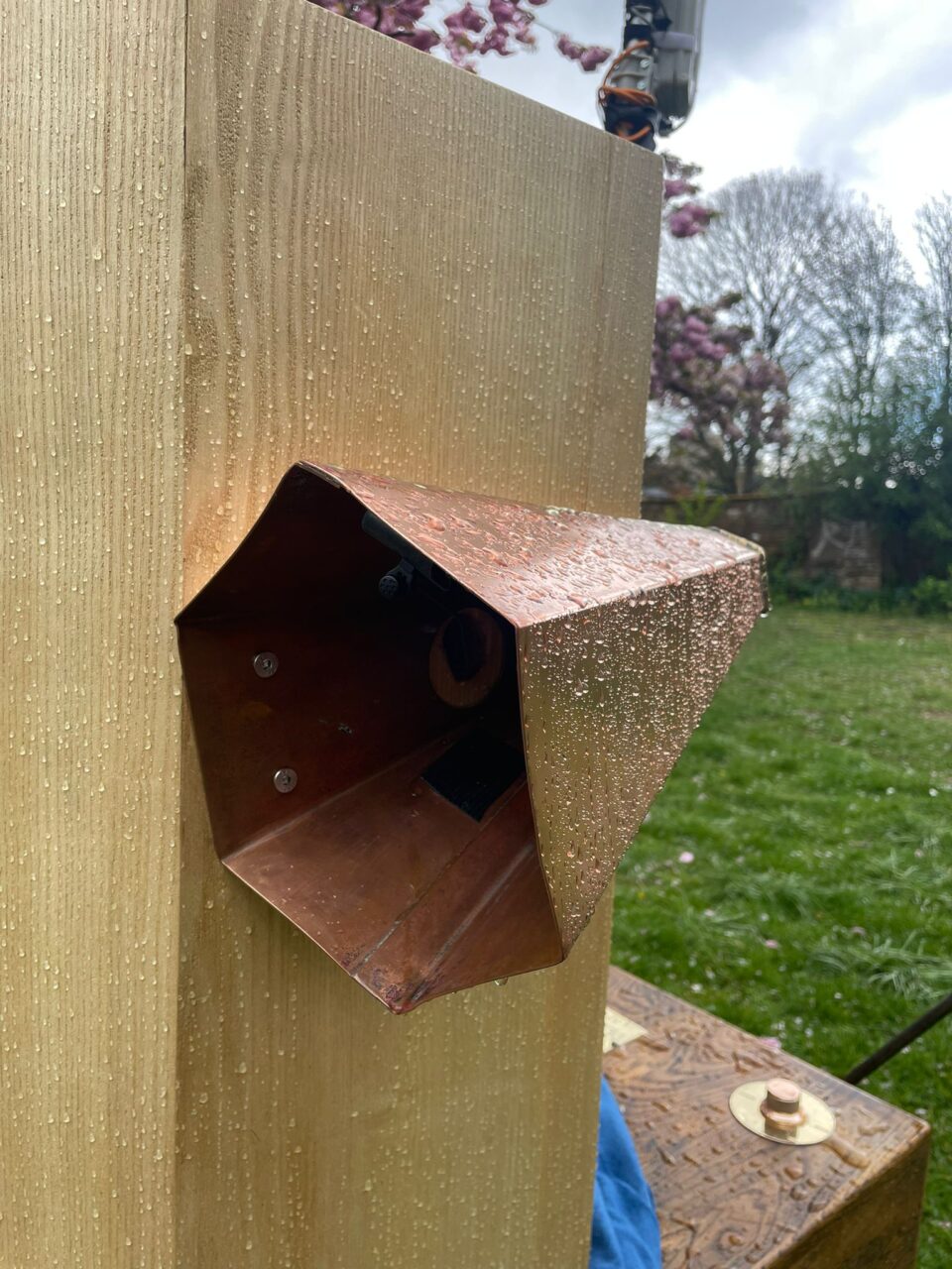 copper trumpet with a tiny microphone on the edge and wooden panels of Future Machine covered in rain drops