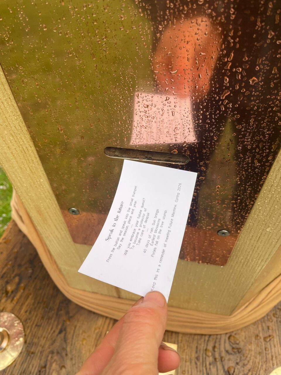 a finger holding a small card with typed text on it next to Future Machine's front copper panel 